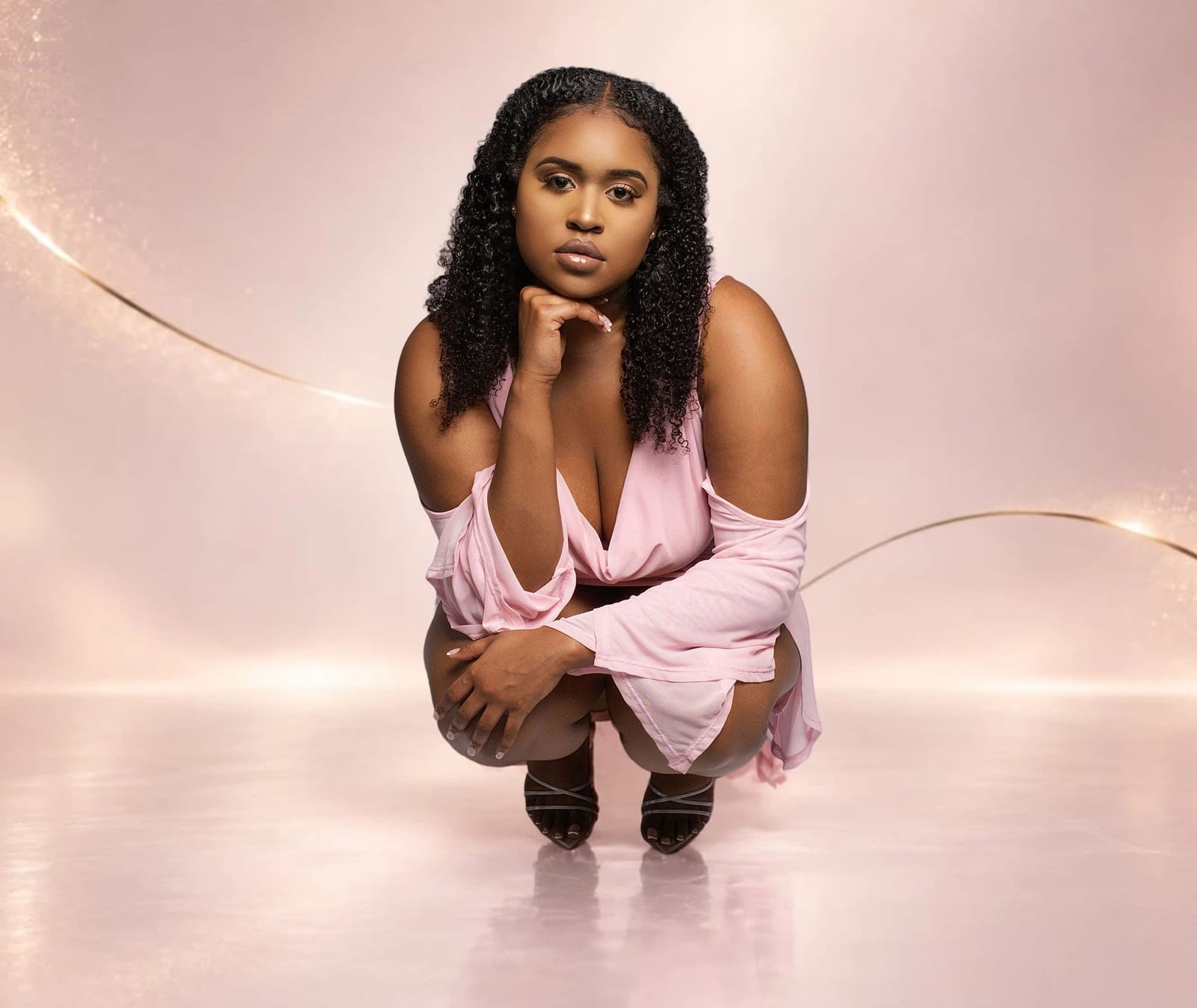 Dr. Jhah Anabirae crouching in a pink dress, chin resting on her hand, looking into the camera.