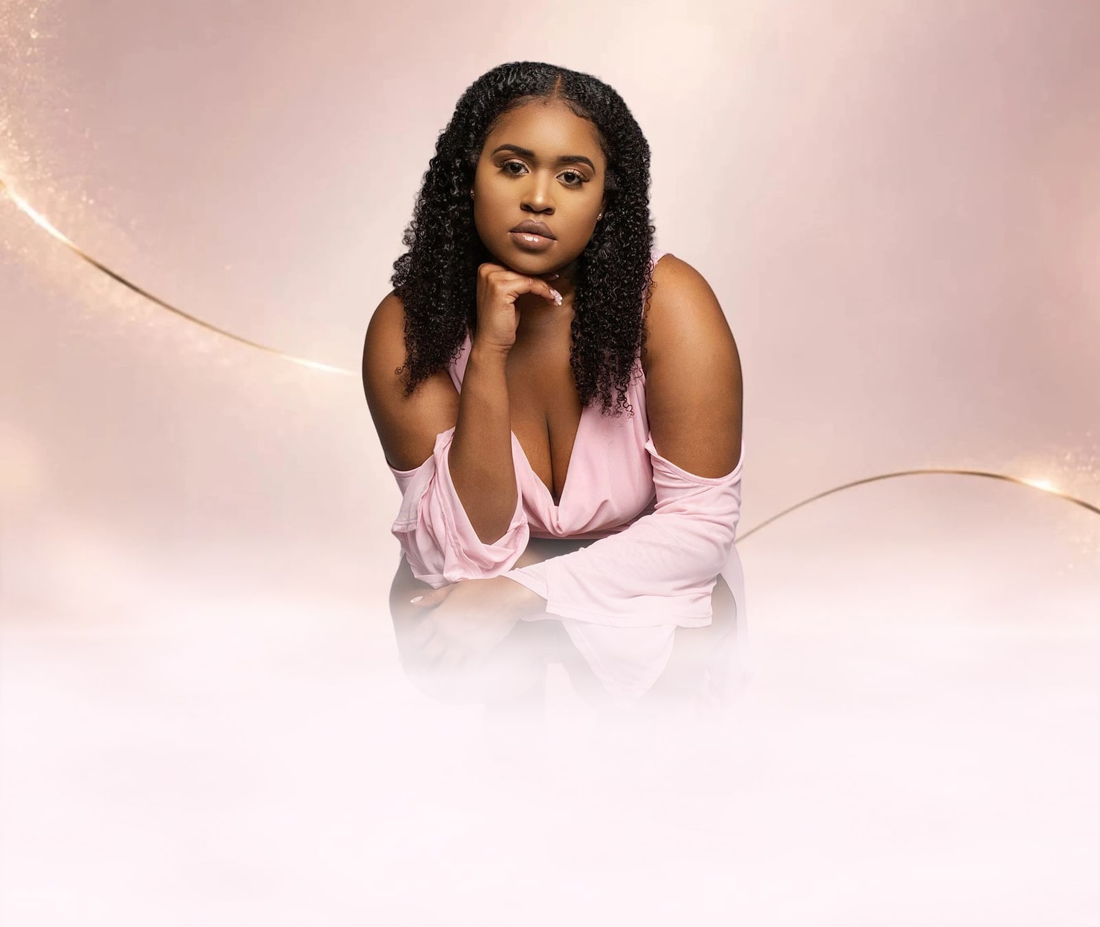 Dr. Jhah Anabirae crouching in a pink dress, chin resting on her hand, looking into the camera.